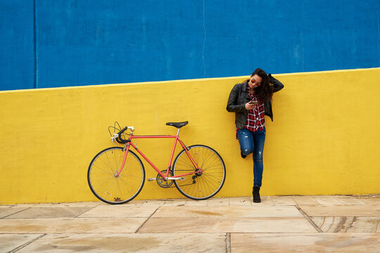 Young woman standing beside his bicycle using her smartphone