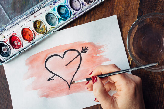 Woman's hand painting a heart in watercolor