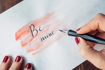 Woman's hand writing ""Be Mine"" on paper