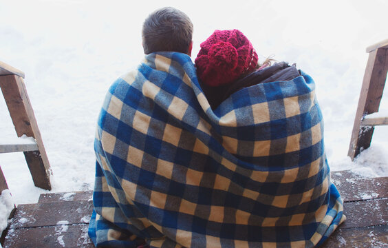 couple cuddled together under blanket sitting on porch on winter day
