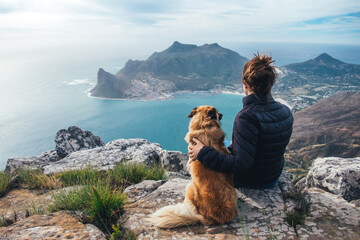 Hiker and pet dog sitting on a rocky mountain summit enjoying a scenic view