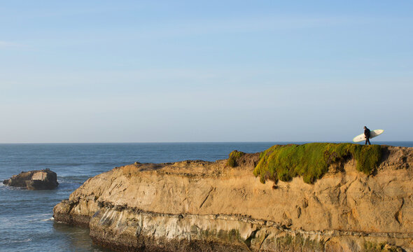 Surfer in a wetsuit walking down a bluff toward the ocean