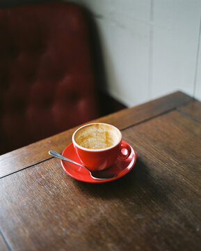 Empty red coffee cup and saucer on a wooden table in a cafe.