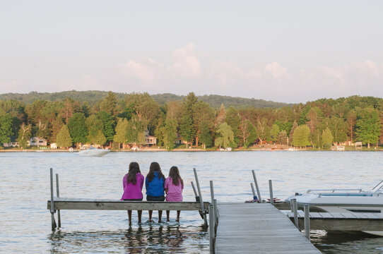 three young women sit at the end of a dock