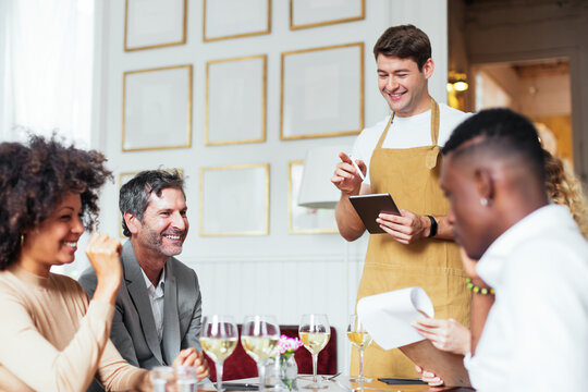 Cheerful waiter taking order from diverse friends