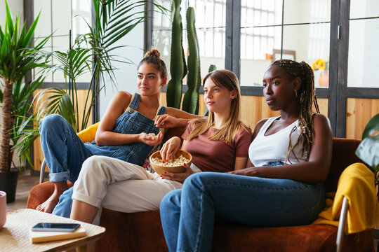 Multiracial teenagers watching film and eating popcorn