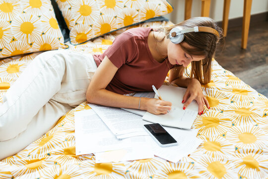 Student listening to music and doing homework on bed