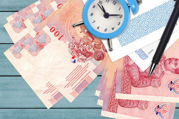 100 Thai Baht bills and alarm clock with pen and envelopes. Tax season concept, payment deadline...
