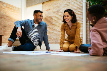 Happy young colleagues sitting on floor and discussing project