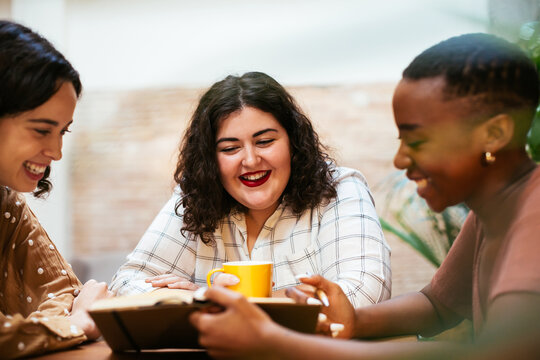Cheerful diverse women discussing notes in creative workplace