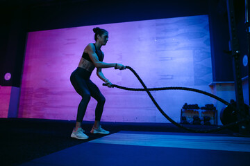 Sweaty athlete woman training hard in dark, moody gym.
