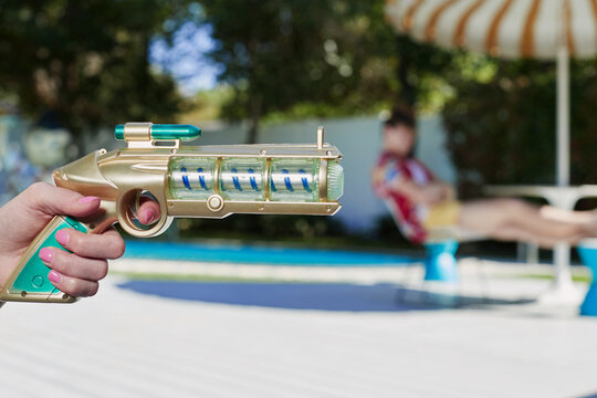 Vintage toy ray gun in woman's hand pointing in the direction of out of focus man in the background.