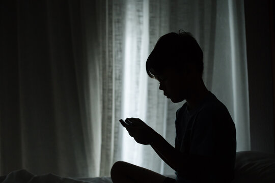 Young boy playing games on mobile phone in dark room.