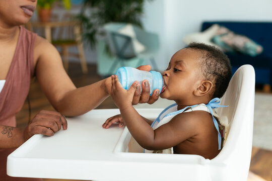 Crop Mother Giving Bottle To Ethnic Baby On Chair