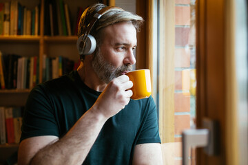 Man listening to music and drinking hot beverage near window