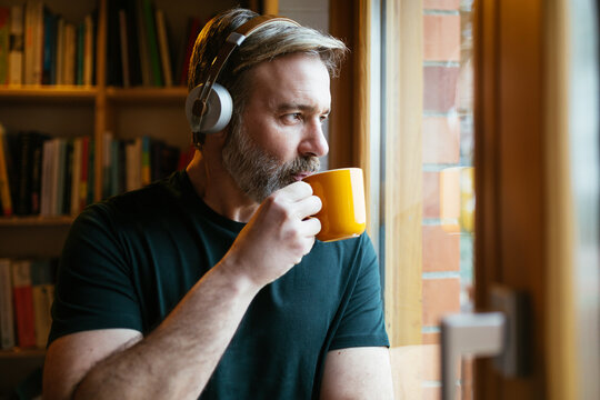 Man listening to music and drinking hot beverage near window