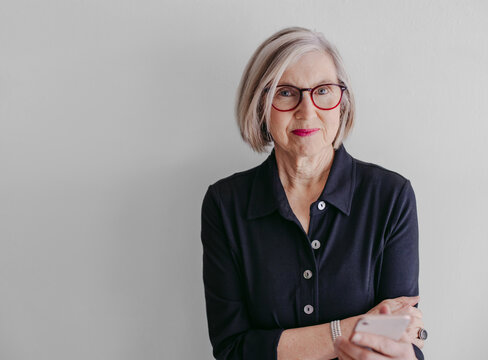 Portrait of mature woman wearing glasses and using mobile phone on seamless white studio background