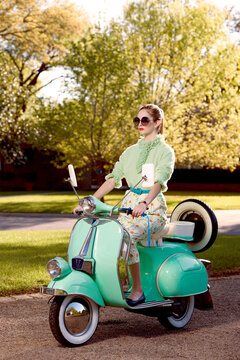 Contemporary vintage inspired shot of a woman riding a Vespa on a sunny afternoon with sunglasses on. 