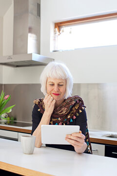 Senior woman in kitchen with coffee using touchpad