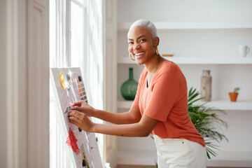 Cheerful ethnic lady making collage on board