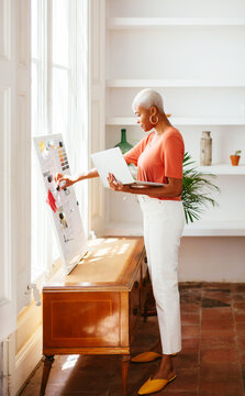 Cheerful ethnic lady making collage on board