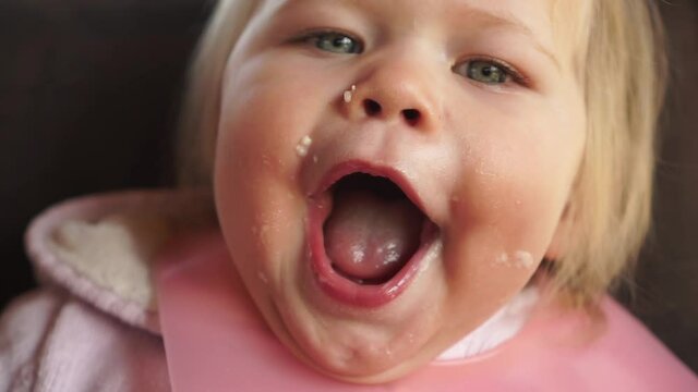 Happy funny chubby baby girl face covered in food mouth wide open hungry waiting for more food positive smiling wide