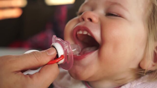 One year old baby girl laugthing playing catching pacifier nipple with her mouth wide open. Children pacifier sucking addiction habbit problem