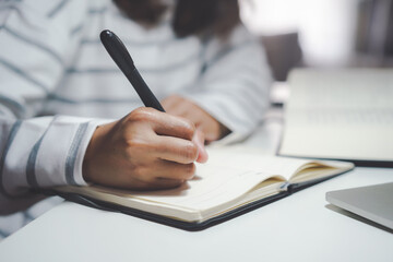 Focus on a woman's hand holding a pen to write something on the notebook at night.