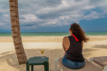 Woman sitting on a cot while contemplating the horizon of the blue sea.