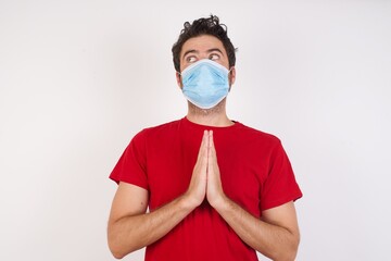Young caucasian man with short hair wearing medical mask standing over isolated white background making up plan in mind holding hands together, setting up an idea. look askance