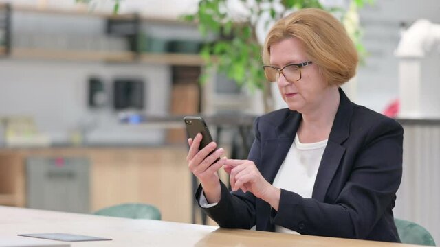 Old Businesswoman with Success on Smartphone in Office 