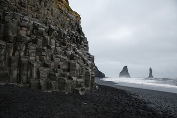 Black sand beach with basalt formations in Reynisfjara, Iceland. Jagged rocks jutting out of sea in...