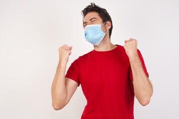 Young caucasian man with short hair wearing medical mask standing over isolated white background celebrating surprised and amazed for success with arms raised and eyes closed. Winner concept.