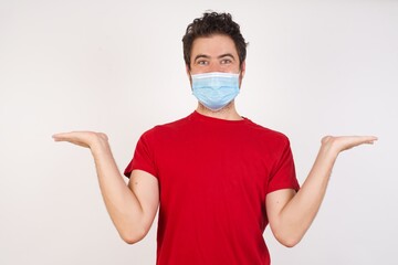 Young caucasian man with short hair wearing medical mask standing over isolated white background holding two palms copy space
