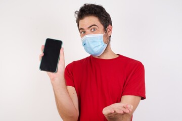 Young caucasian man with short hair wearing medical mask standing over isolated white background with a mobile. presenting smartphone