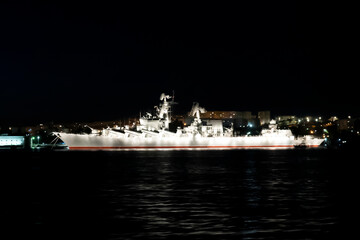Military ship in the seaport at night with illumination.