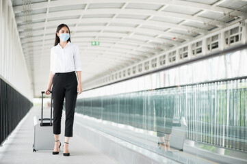 Young asian business woman wearing protection mask walking in airport terminal with trolley bag. Beautiful female travel in city downtown.