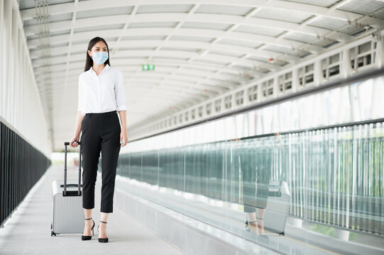 Young Asian Business Woman Wearing Protection Mask Walking In Airport Terminal With Trolley Bag. Beautiful Female Travel In City Downtown.