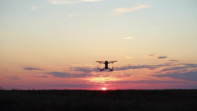 Black drone flying in sunset evening sky. Beautiful fiery cloudy landscape over the horizon. Futuristic technology generation. Agriculture equipment gadget. Monitoring system. Summer setting sun. 4K