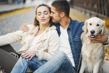 brunette couple walking their golden retriever dog in the city on a sunny autumn day