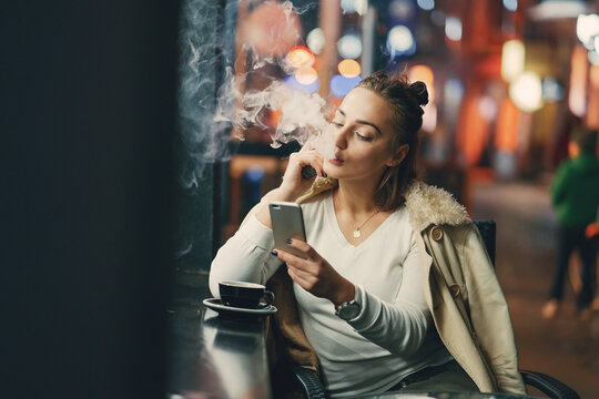 girl drinking coffee and using her phone outside a cafe during the evening