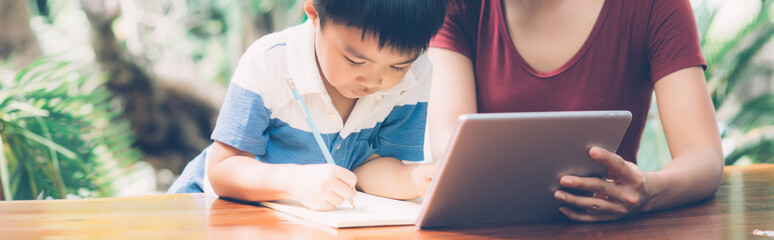 Son using digital tablet computer for study and learn to internet online with mother together,...