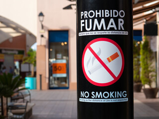 In a pedestrian zone, a white sign on a black foil on a pillar prohibits smoking in this area. The...
