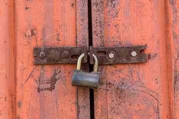Padlock on metal gate hinges. old orange paint with a red tint, rust. Closed door concept.