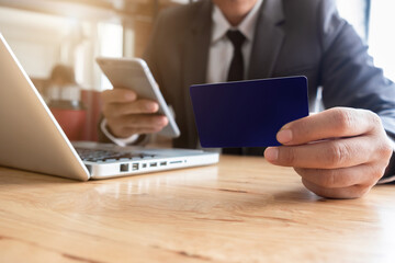 Businessman hand holding credit card and use laptop and smartphone in office.
