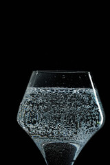 Mineral water is poured into a glass. Black background.
