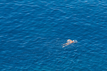 man swims along the rocks in clear water, aerial view