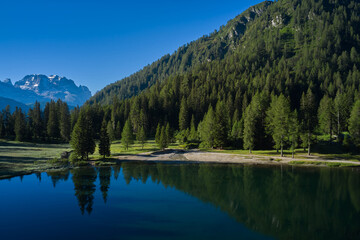 Reflections in water. Sun on a crystal blue sky. Reflections of trees, mountains, sky in a mountain lake. Early morning in the Alps. Aerial view.