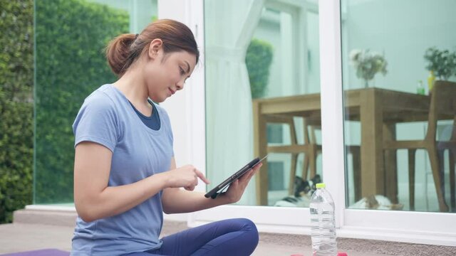 Asian sporty woman choosing online tutorials workout and yoga on internet channel in taplet device before exercise and stretching. Activity during quarantine and social distance new normal concept.