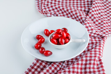 Cornel berries in scoop and plate on white and picnic cloth background. high angle view.